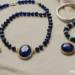 A collection of dark blue crystal jewelry, including a lapis lazuli necklace, sodalite bracelet, and sapphire ring, arranged on a linen cloth.
