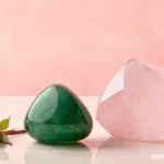 A polished green Jade stone next to a soft pink Rose Quartz crystal on a clean, light background, symbolizing love and harmony.